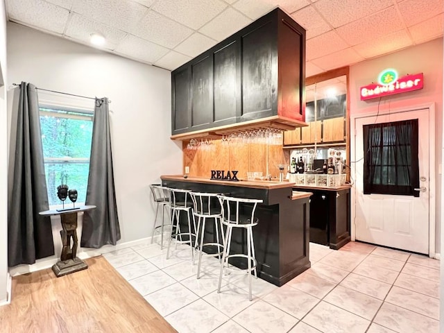 kitchen featuring a breakfast bar area, light tile patterned floors, kitchen peninsula, and a drop ceiling