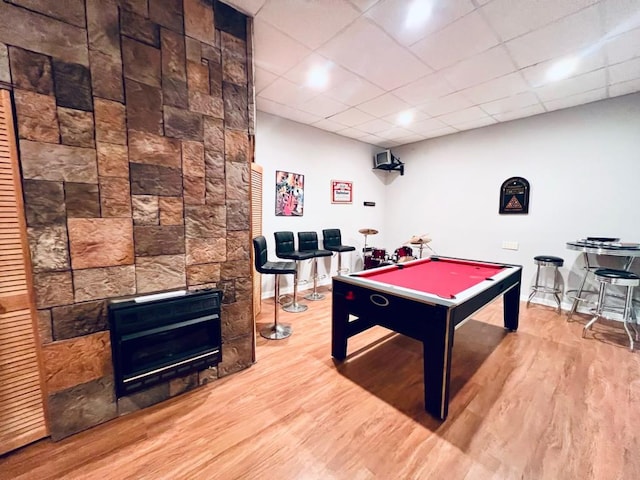 rec room featuring hardwood / wood-style flooring, billiards, a paneled ceiling, and a stone fireplace