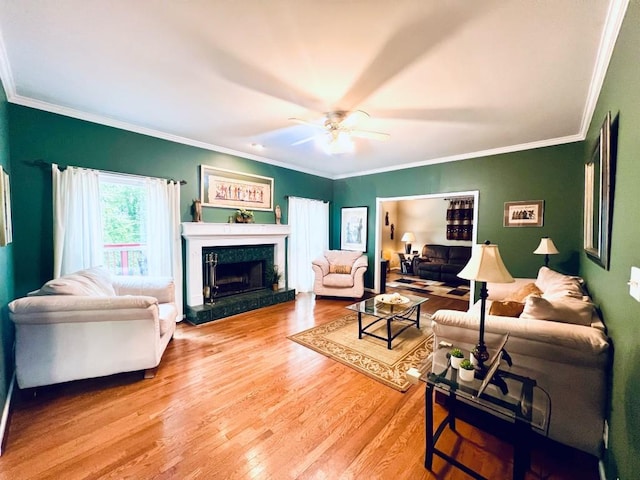 living room featuring light wood-type flooring, ceiling fan, a fireplace, and crown molding