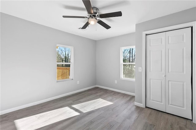 unfurnished bedroom featuring multiple windows, ceiling fan, light hardwood / wood-style floors, and a closet