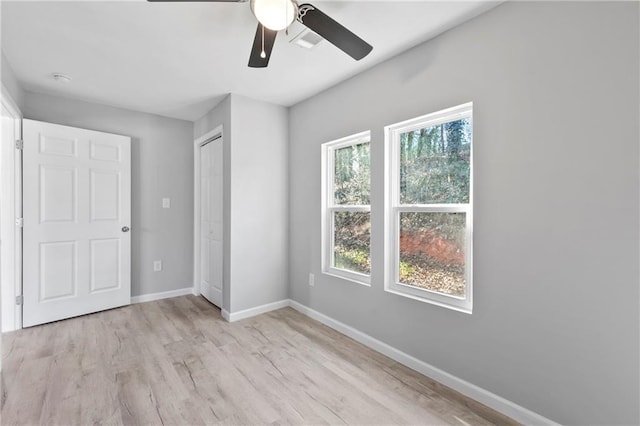 unfurnished bedroom featuring multiple windows, light wood-type flooring, ceiling fan, and a closet