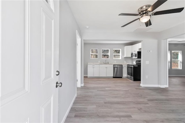 interior space with sink, ceiling fan, stainless steel appliances, light hardwood / wood-style floors, and white cabinets