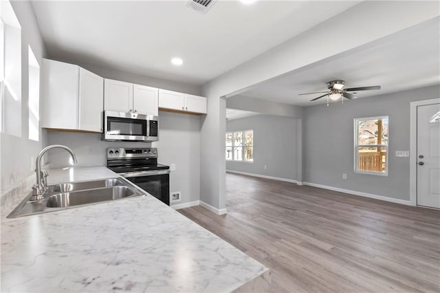 kitchen with sink, white cabinetry, light wood-type flooring, stainless steel appliances, and light stone countertops