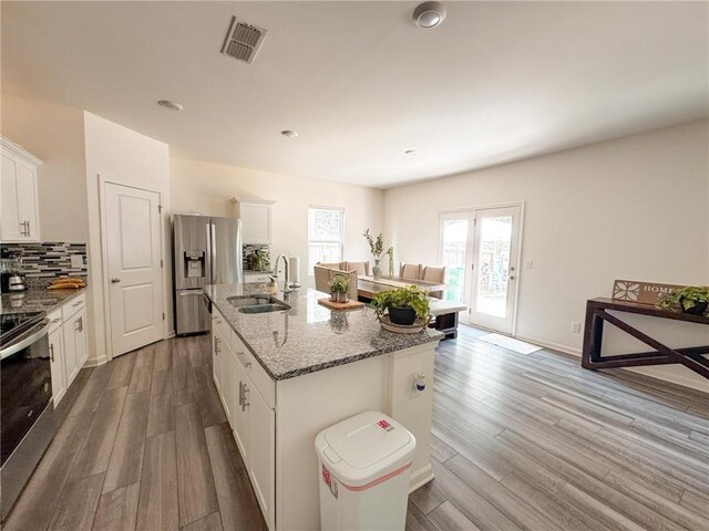 kitchen featuring appliances with stainless steel finishes, light stone counters, sink, white cabinets, and an island with sink