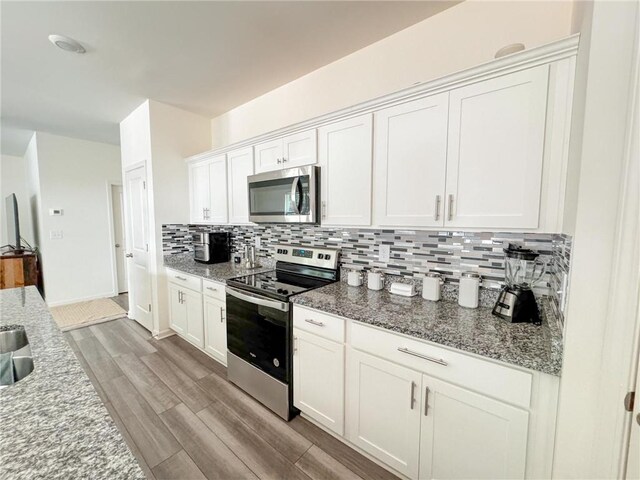 kitchen with light stone countertops, stainless steel appliances, backsplash, light hardwood / wood-style floors, and white cabinets