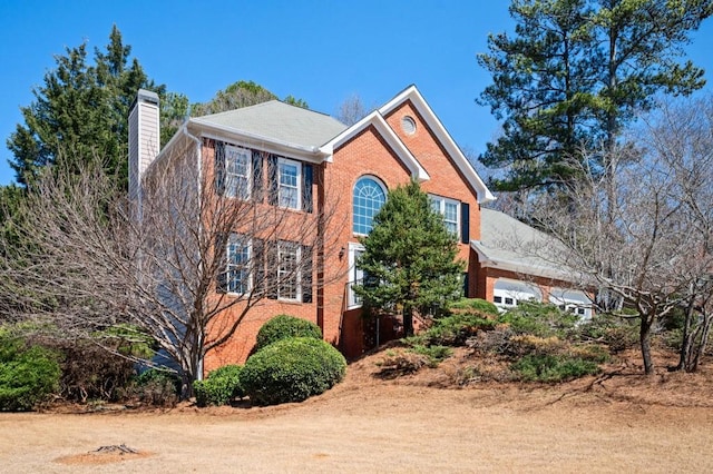 colonial inspired home featuring brick siding, an attached garage, and a chimney