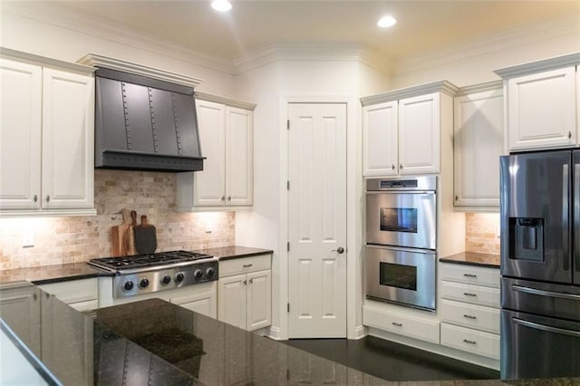 kitchen featuring wall chimney range hood, crown molding, appliances with stainless steel finishes, white cabinetry, and decorative backsplash