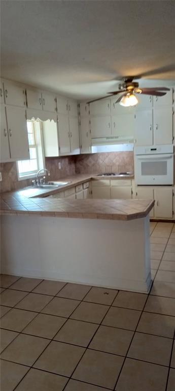 kitchen featuring sink, light tile patterned floors, white oven, white cabinetry, and backsplash