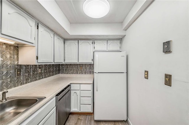 kitchen featuring freestanding refrigerator, stainless steel dishwasher, a sink, decorative backsplash, and light countertops