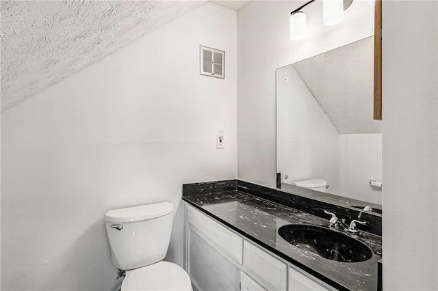 bathroom featuring toilet, lofted ceiling, a textured ceiling, and vanity