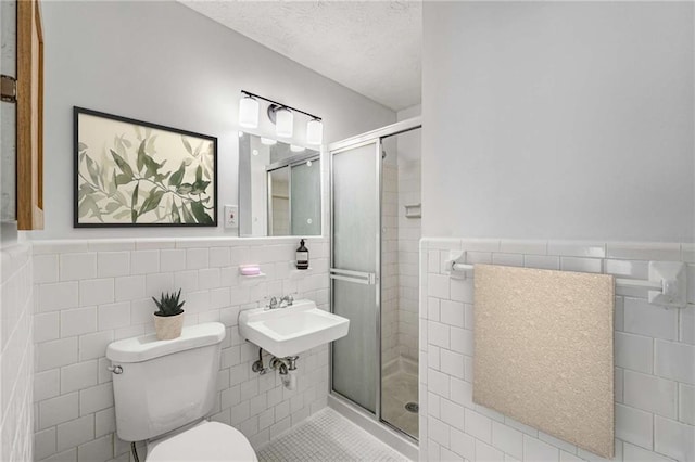 bathroom featuring tile walls, a stall shower, a wainscoted wall, toilet, and tile patterned flooring