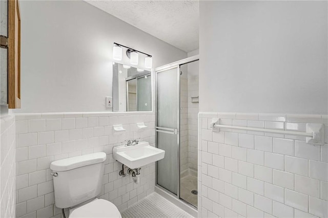full bath featuring tile walls, a stall shower, a wainscoted wall, toilet, and a textured ceiling