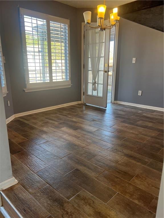 empty room with an inviting chandelier, dark wood finished floors, and baseboards