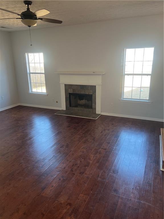 unfurnished living room with dark wood-style floors, ceiling fan, a fireplace, and baseboards