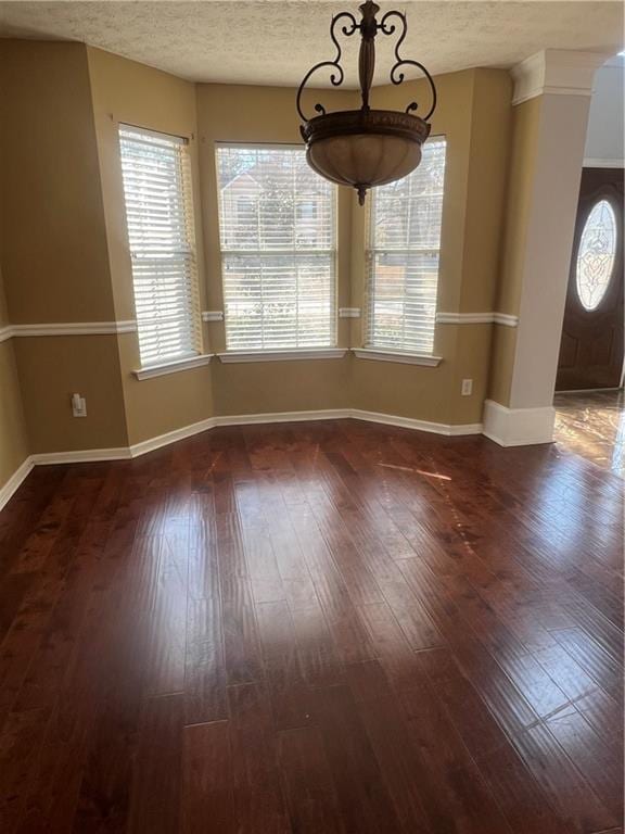 unfurnished dining area featuring a textured ceiling, wood-type flooring, and baseboards