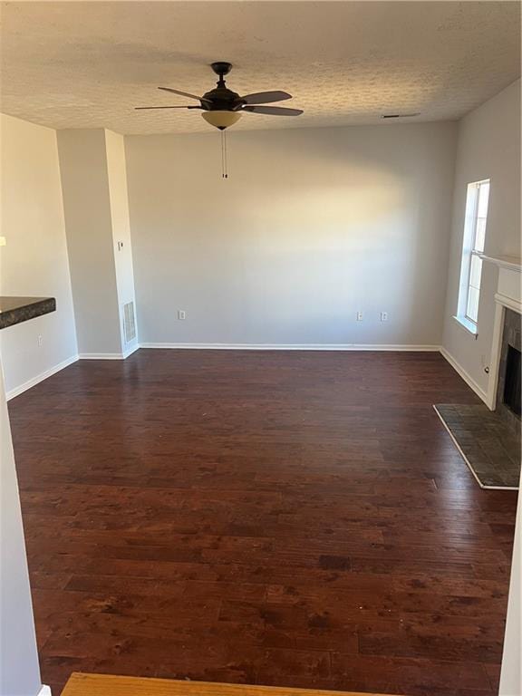 unfurnished room with ceiling fan, a textured ceiling, baseboards, dark wood-style floors, and a tiled fireplace