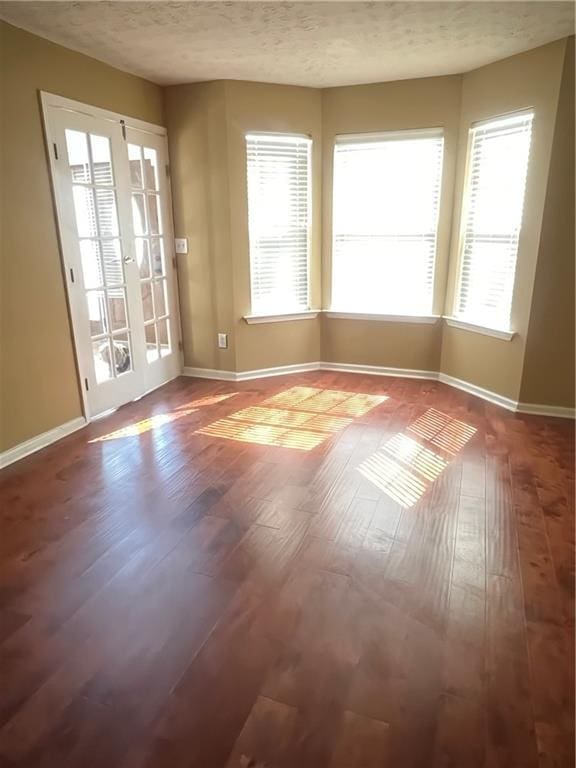 spare room with a textured ceiling, wood-type flooring, and baseboards