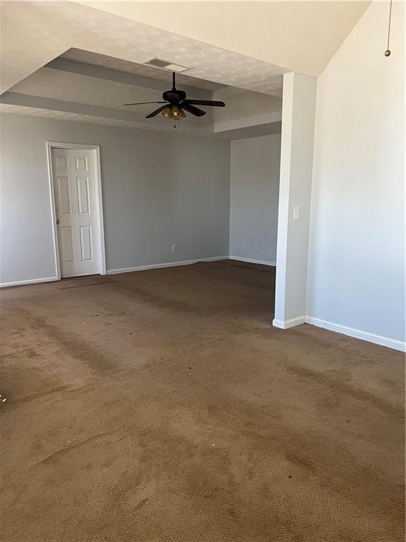 spare room with baseboards, dark colored carpet, and a raised ceiling