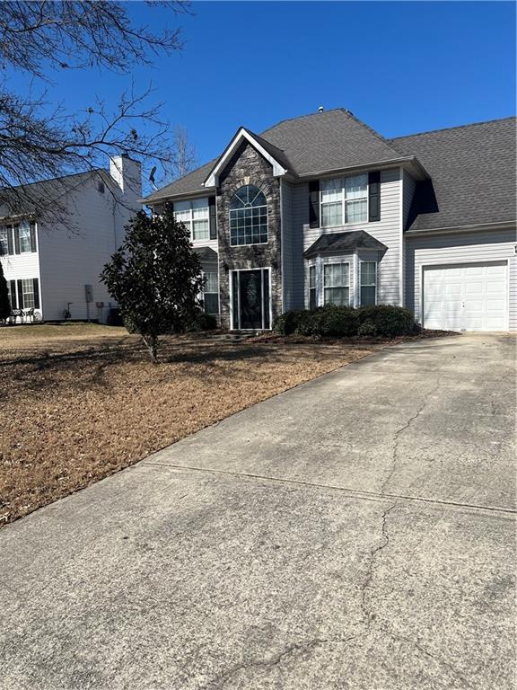 traditional home with stone siding, concrete driveway, roof with shingles, and an attached garage