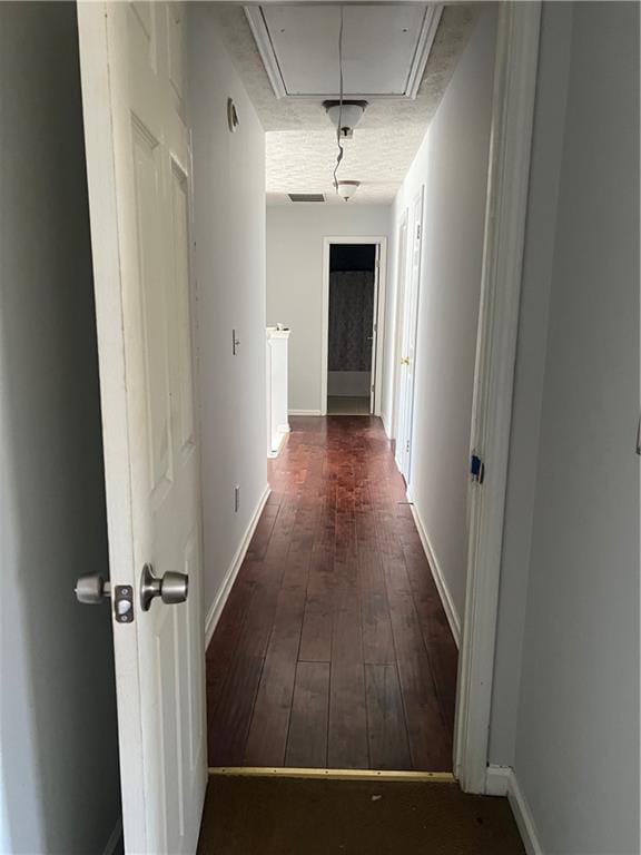 hall with dark wood-type flooring, attic access, and baseboards