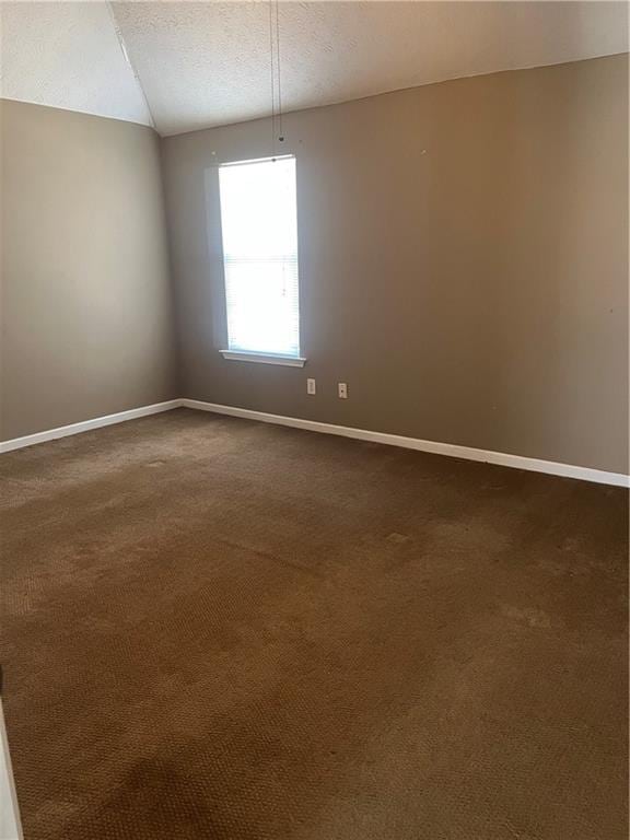 unfurnished room featuring baseboards, dark carpet, vaulted ceiling, and a textured ceiling