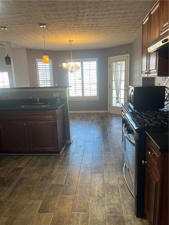 kitchen featuring stainless steel gas range oven, dark countertops, dark wood-style floors, black microwave, and a sink