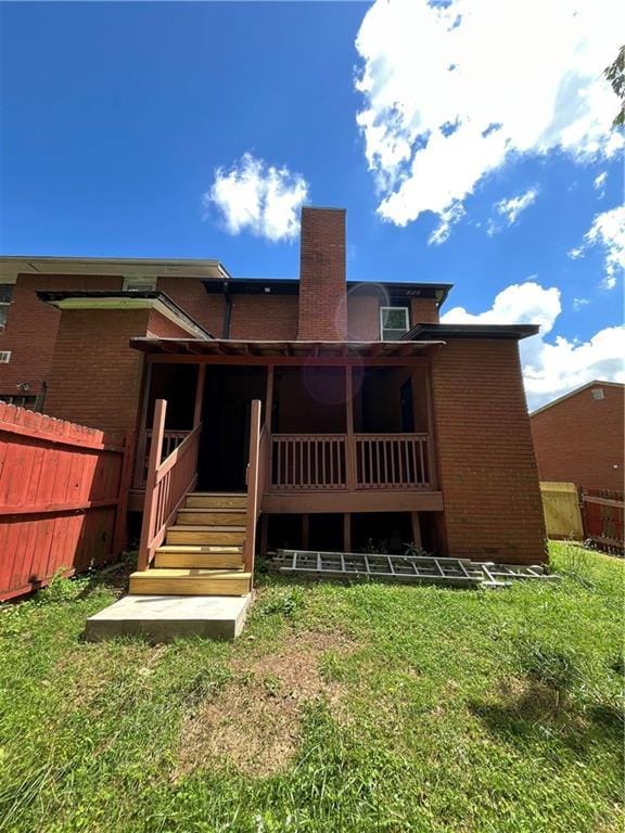 rear view of house featuring fence, a deck, a chimney, brick siding, and a lawn