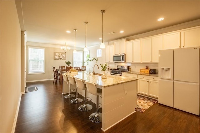 kitchen featuring stainless steel appliances, an island with sink, white cabinetry, and decorative light fixtures