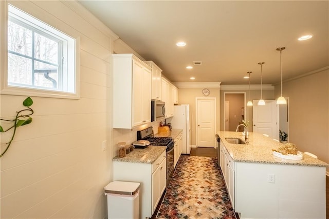 kitchen with appliances with stainless steel finishes, white cabinetry, hanging light fixtures, light stone countertops, and a center island with sink