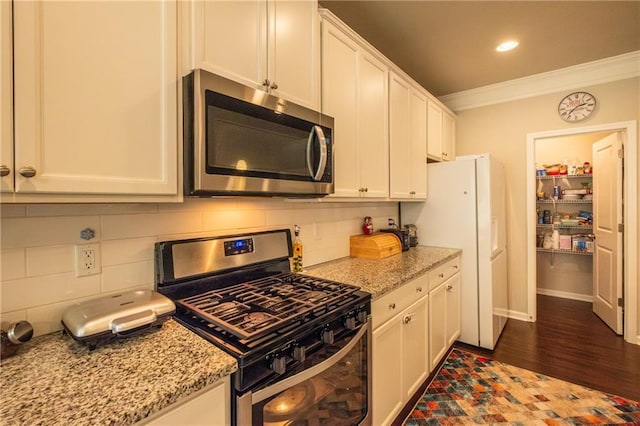 kitchen featuring appliances with stainless steel finishes, white cabinetry, decorative backsplash, crown molding, and light stone countertops