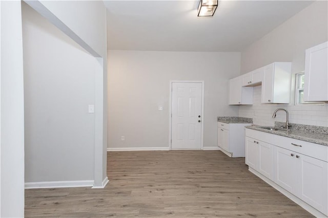 kitchen featuring sink, white cabinetry, tasteful backsplash, light stone countertops, and light wood-type flooring