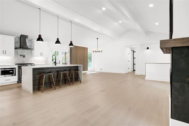 kitchen with a breakfast bar area, electric range oven, wall chimney range hood, a kitchen island with sink, and white cabinets