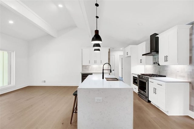 kitchen with pendant lighting, high end stove, white cabinetry, sink, and wall chimney range hood