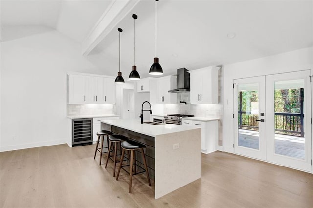 kitchen with white cabinetry, an island with sink, sink, high end stainless steel range, and wall chimney exhaust hood