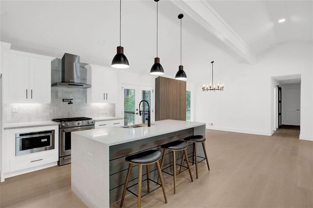 kitchen with sink, appliances with stainless steel finishes, an island with sink, white cabinets, and wall chimney exhaust hood