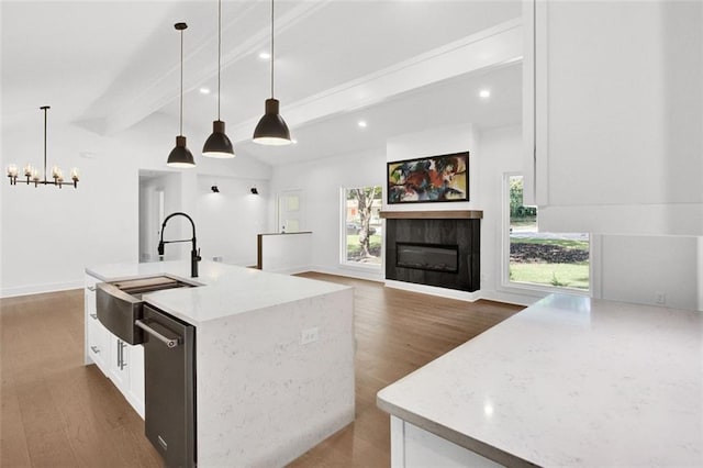 kitchen featuring hanging light fixtures, light stone countertops, an island with sink, and a tile fireplace