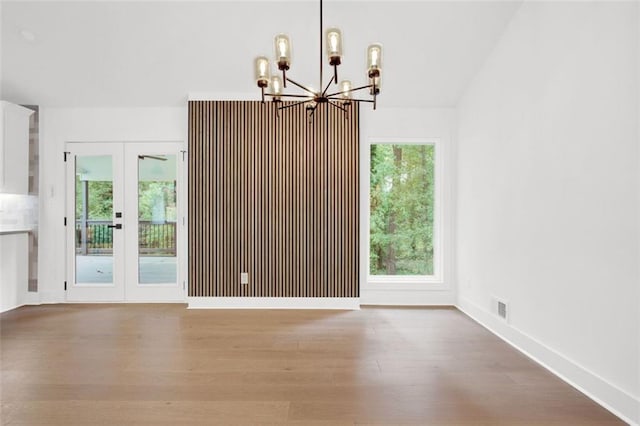 unfurnished dining area featuring hardwood / wood-style flooring, french doors, and a chandelier