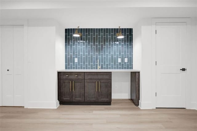 bar with decorative light fixtures, dark brown cabinets, and light hardwood / wood-style floors