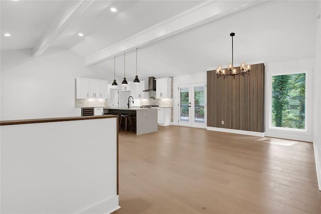 kitchen featuring a kitchen island with sink, wall chimney range hood, white cabinetry, and decorative light fixtures