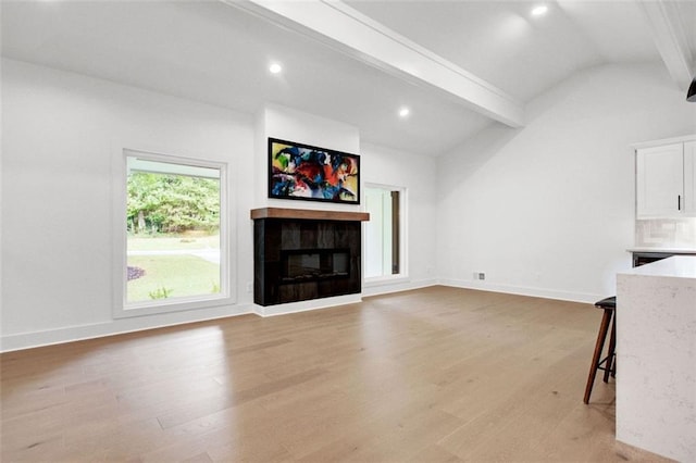 living room featuring a tiled fireplace, vaulted ceiling with beams, and light wood-type flooring