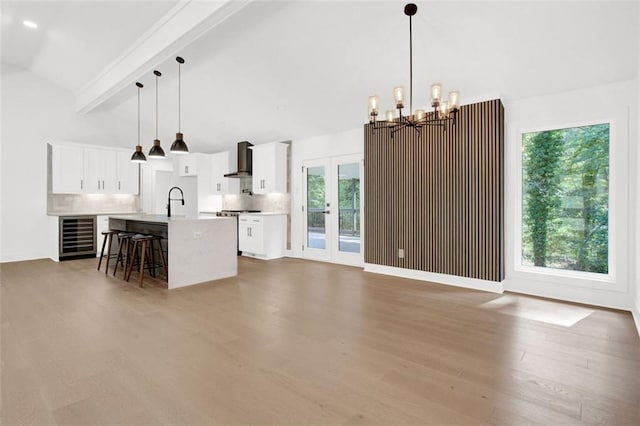 kitchen with pendant lighting, white cabinetry, beverage cooler, a center island with sink, and wall chimney exhaust hood