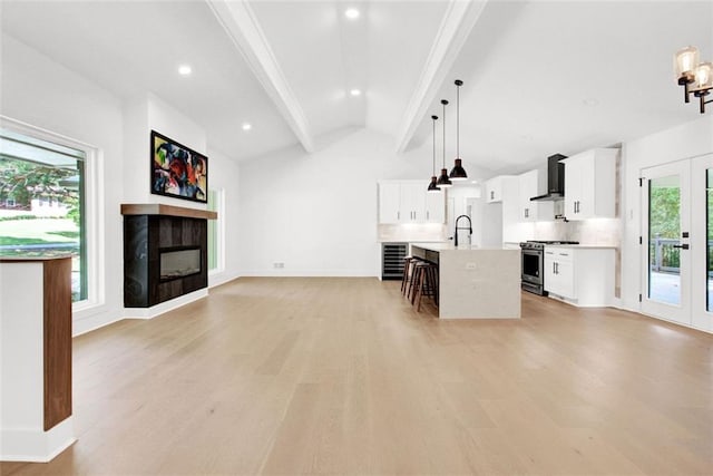 interior space featuring pendant lighting, wall chimney range hood, a kitchen island with sink, gas stove, and white cabinets