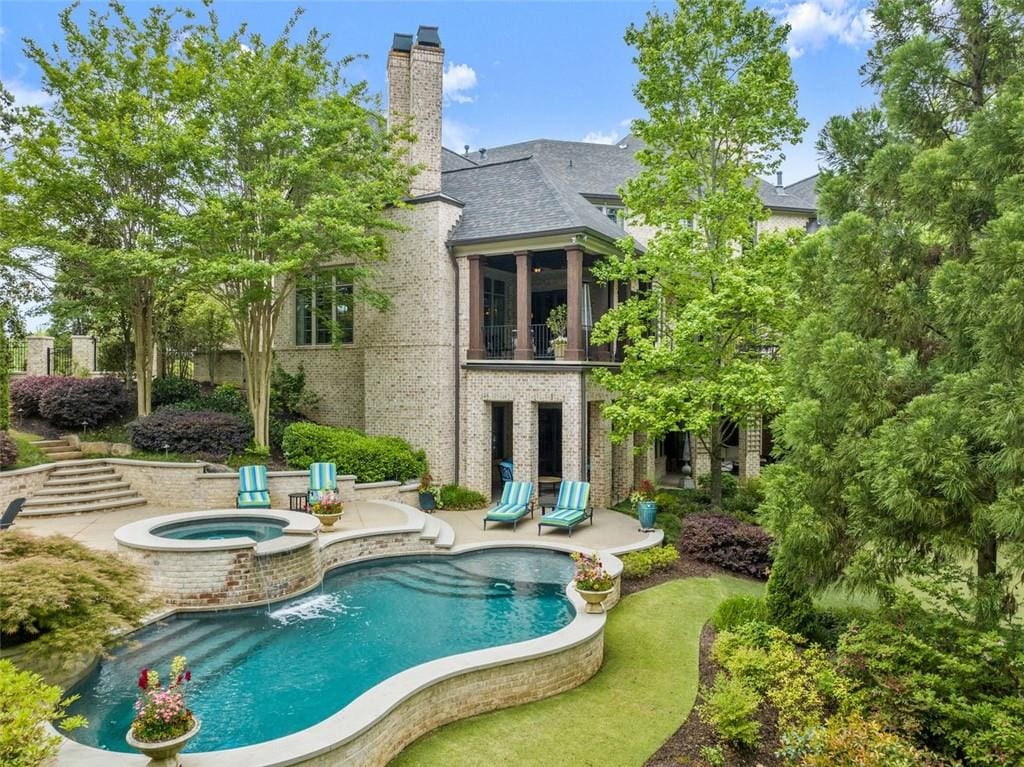 rear view of house with an in ground hot tub, a balcony, and a patio area