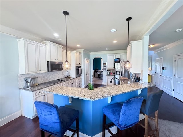 kitchen with white cabinets, appliances with stainless steel finishes, a kitchen bar, hanging light fixtures, and kitchen peninsula