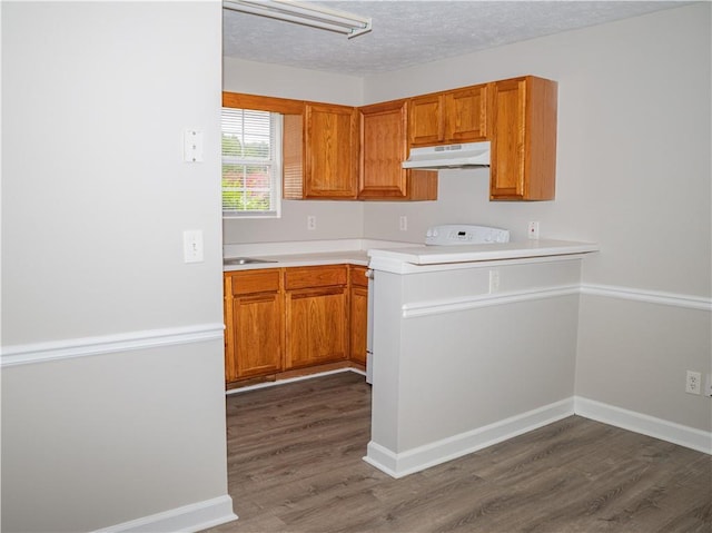 kitchen featuring under cabinet range hood, stove, light countertops, brown cabinets, and dark wood finished floors