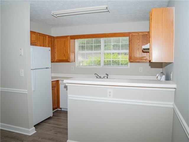 kitchen featuring dark wood-style flooring, brown cabinets, light countertops, a textured ceiling, and white appliances