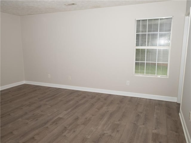 spare room with a textured ceiling, baseboards, and dark wood-type flooring