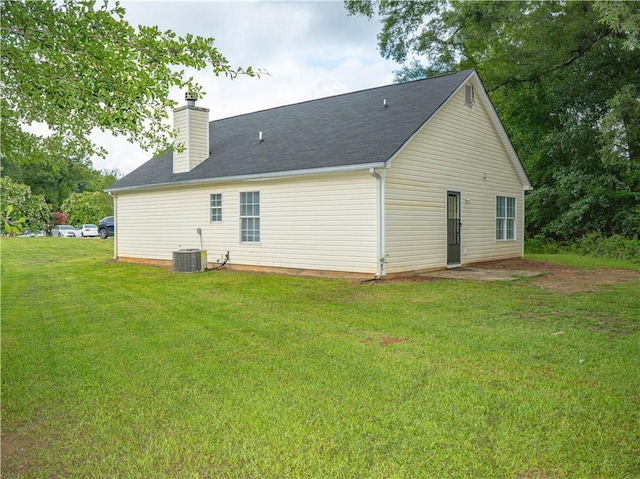 back of property featuring central AC unit, a lawn, and a chimney