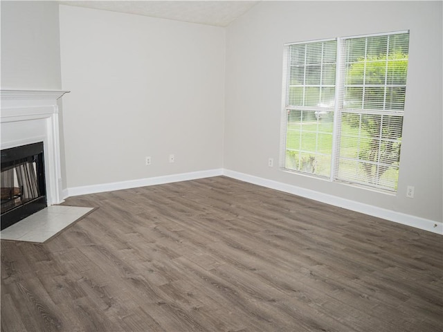 unfurnished living room featuring lofted ceiling, wood finished floors, a fireplace with flush hearth, and baseboards