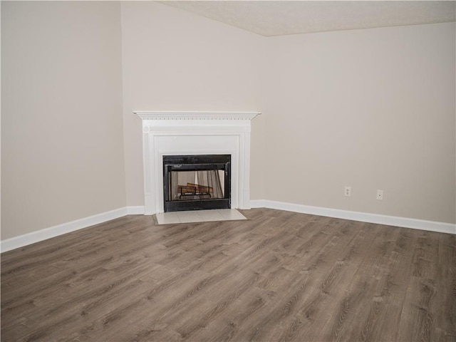 unfurnished living room featuring wood finished floors, a fireplace with flush hearth, and baseboards